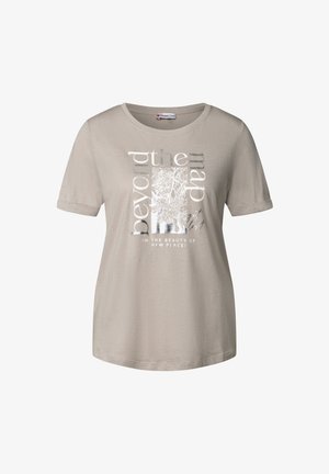 Beżowy t-shirt z krótkim rękawem i okrągłym dekoltem. Ma graficzny nadruk z srebrnymi akcentami oraz tekst: "poza mapą" i "w pięknie nowych miejsc".