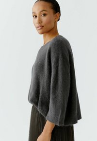 Dark grey, loose-fitting sweater made of soft, fluffy material. Features a wide neckline and three-quarter length sleeves.