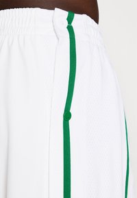 Vita atletiska shorts i meshmaterial, med en grön sidostrip och knäppknapp stängning i midjan.