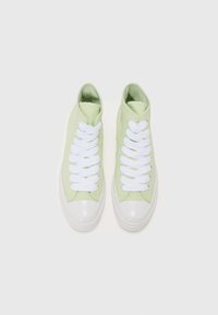 Sneakers înalte din pânză verde, cu șireturi albe și capace de cauciuc pentru degete. Textură netedă, cu o formă rotunjită și un design minimalist.