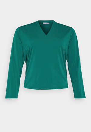 Top verde cu mânecă lungă și decupaj în V. Fabricat dintr-un material moale, având o croială confortabilă și un tiv drept. Fără modele sau accente vizibile.