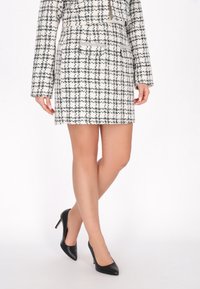 Tweed jakkesæt med et sort-hvidt ternet mønster, der har en tætsiddende jakke og en miniskirt. Sættes sammen med sorte højhælede sko.