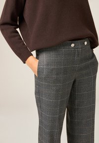 Gray plaid trousers feature a smooth texture, with a high waist and twin silver button accents at the front. Add a relaxed brown top.
