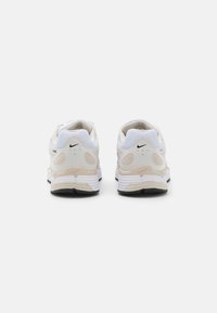 Scarpe sportive bianche e beige con tessuto in rete, colli imbottiti, suole tonde e sottili accenti del logo sul lato e sul tallone.