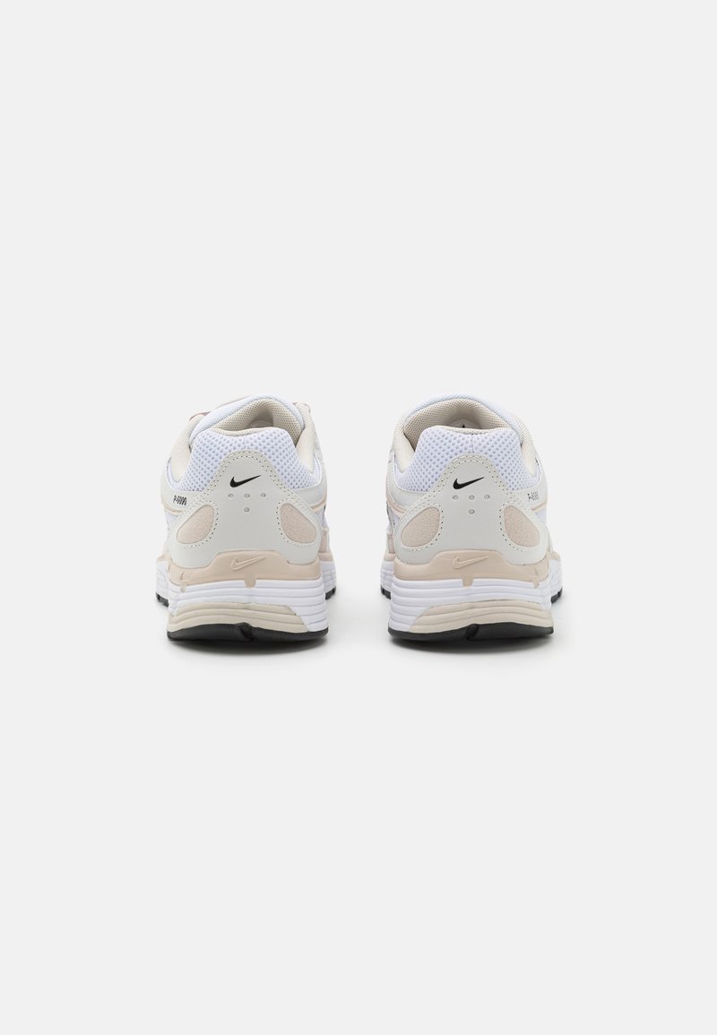 Weiße und beige Sportschuhe aus Mesh-Gewebe, mit gepolstertem Kragen, runden Sohlen und dezenten Logo-Akzenten an der Seite und der Ferse.