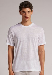 Weißes T-Shirt mit kurzen Ärmeln aus leichtem, leicht strukturiertem Stoff. Verfügt über einen klassischen Rundhalsausschnitt und eine lockere Passform.
