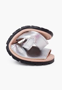 Silberne, metallische Sandalen mit flachem Design, strukturiertem Riemen und Gummisohle. Die Sandalen werden in gefalteter Position gezeigt.