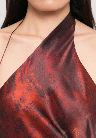 Close-up of a person wearing a red and black marbled halter top with exposed shoulders and long dark hair.