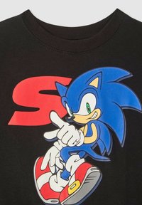 Felpa nera con grafica colorata di un personaggio riccio blu con occhi verdi, scarpe rosse e un grande sfondo rosso a forma di "S".