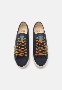 Baskets en toile navy avec des lacets orange, ornées de patchs brodés et d'une semelle en caoutchouc crème, offrant un contraste texturé.