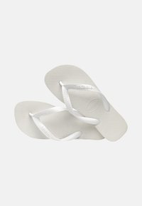 Witte teenslippers met verhoogde zolen en dunne banden. Het materiaal lijkt rubberachtig met een merklogo zichtbaar op een band.
