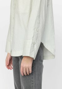 Lys cremefarvet skjorte med tynde lodrette striber, med en brystlomme, opadvendte manchetter og en afslappet pasform. Sammen med grå jeans.