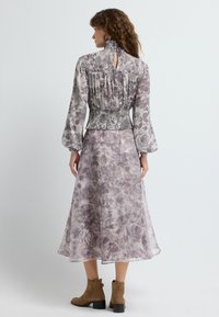 Bluse med blomstermønster, høj hals og smocket talje, parret med en luftig midikjole i nuancer af lavendel, båret med brune ankelstøvler.