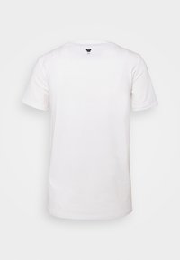 Camiseta blanca de algodón con mangas cortas, escote redondo y un pequeño logo de mariposa negra en la parte de atrás, justo debajo del escote.