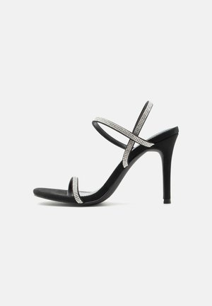 Black high-heeled sandal with thin straps adorned with small rhinestones crossing over foot and ankle on a white background.