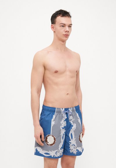 Shorts de bain bleus et gris en tissu léger, ornés d'un motif floral et de deux accents décoratifs ronds à l'avant.