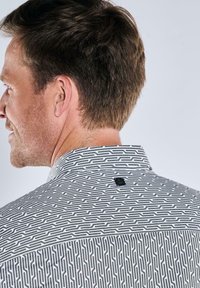 Gemustertes kurzärmliges Hemd in Schwarz und Weiß mit einem geometrischen Design, das einen Stehkragen und ein kleines Markenlogo auf der Rückseite aufweist.