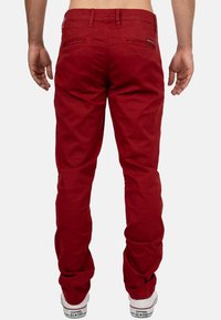 Pantaloni rossi in cotone con taglio slim. Presentano passanti per cintura, due tasche posteriori e orli risvoltati. Abbinati a sneakers bianche.