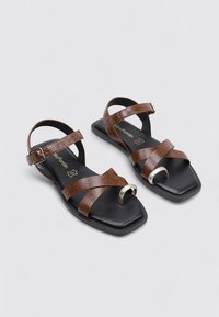 Sandalias de imitación de cuero marrón con un acabado texturizado, que cuentan con una punta abierta, correas cruzadas y un acento de metal plateado. Suela de forma cuadrada.