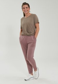 Ljusbrun kortärmad topp med vriden framdesign, kombinerad med mjuka, ljusrosa joggers med fickor, bärs tillsammans med vita sneakers.