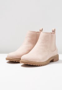 Botines de ante rosa con paneles elásticos en los laterales, punteras redondeadas y suela de goma gruesa y texturizada. Pequeñas pestañas en la parte trasera para facilitar su colocación.