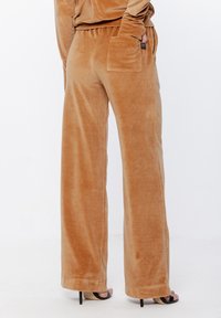 Welurowe spodnie o szerokim kroju w ciepłym kolorze karmelowym, o gładkiej fakturze. Posiadają tylną kieszeń i widoczne szwy u dołu.