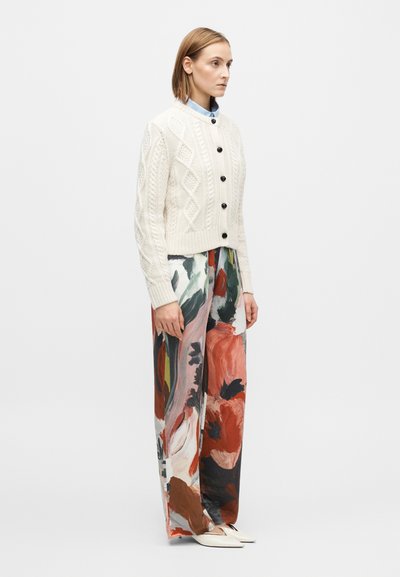 Cardigan en maille crème avec des motifs en losange et des boutons noirs, associé à un pantalon à jambes larges avec un motif floral abstrait coloré.