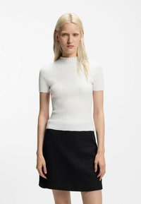 Top bianco a maniche corte a coste con collo alto, abbinato a una minigonna nera dalla trama lavorata. Design semplice e silhouette aderente.