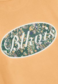 T-shirt en coton orange avec un imprimé paisley vert circulaire et le texte blanc "Blkots" dans une police décontractée. Texture lisse avec une coupe décontractée.