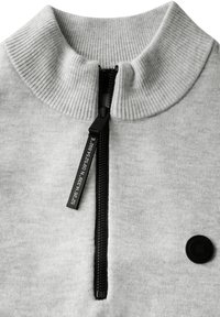 Grå tröja med hög ribbad krage, svart dragkedja och etikett. Har en rund svart knapp och mjukt, texturerat tyg.