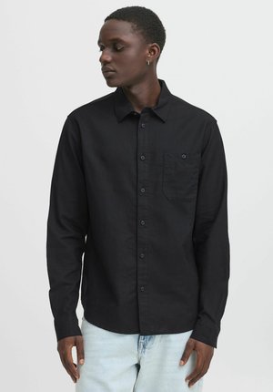 Zwarte overhemd met knopen, gemaakt van gladde stof, met een borstzak, lange mouwen en een klassieke kraag. Draag het met lichtblauwe jeans.