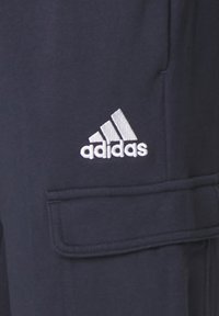 Pantaloni cargo blu navy realizzati in tessuto misto cotone, dotati di una tasca laterale e di un logo Adidas bianco ricamato sulla coscia sinistra.