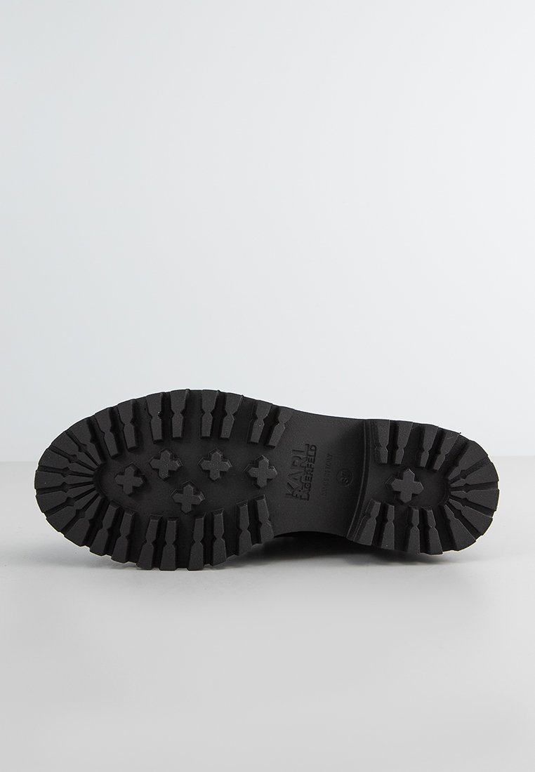 Semelle en caoutchouc noir avec des rainures profondes et des motifs croisés ; présente un logo de marque embossé "KARL" près du talon. Design plat et robuste.