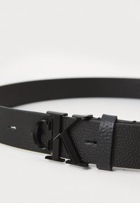 Schwarzer Ledergürtel mit strukturiertem Finish, eleganter Schnalle mit eingeprägtem "CK"-Logo und verstellbaren Löchern für die Anpassung.
