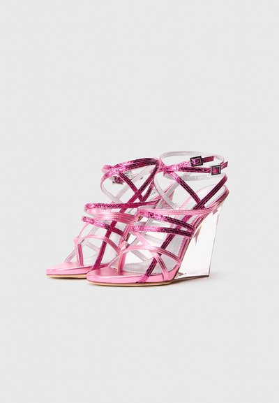 Rozā augstpapēžu platformas sandales ar krustveida metāliskām siksnām un divām potīšu sprādzēm uz baltas fona.