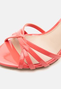 Σανδάλι από δερμάτινο βερνίκι σε κοραλλί ροζ χρώμα με πολλά λεπτά διασταυρωμένα λουράκια και μπεζ μαλακό εσωτερικό πάτο.