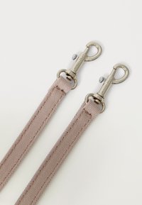 Canvasrem i mjuk rosa med silverfärgad metallutrustning. Har två vridbara krokodilklämmor i varje ände och sömdekoration längs kanterna.