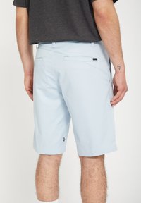 Light blue shorts made from a smooth fabric, featuring back pockets, a small logo near the hem, and a relaxed fit.