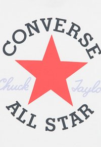Λευκό ύφασμα με ένα μεγάλο κόκκινο αστέρι στο κέντρο. Το κείμενο πάνω από το αστέρι γράφει "CONVERSE" και κάτω γράφει "ALL STAR" με έντονα μαύρα γράμματα. Το όνομα "Chuck Taylor" είναι σε ανοιχτό μπλε χρώμα.