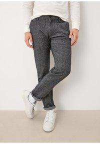 Szare w kratę spodnie wykonane z teksturowanej tkaniny, w wąskim kroju, z podwiniętymi nogawkami, noszone z białymi trampkami i skarpetkami do kostek.