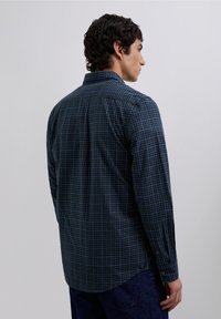 Camisa de manga larga a cuadros en azul marino y verde, de tela de algodón, con puños abotonados y un dobladillo curvado, vista desde la parte trasera.