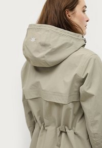 Lichtbeige, lichtgewicht jack met een trekkoord in de taille, capuchon en geborduurd logo op de rug. Glad textuur met een utilitair ontwerp.