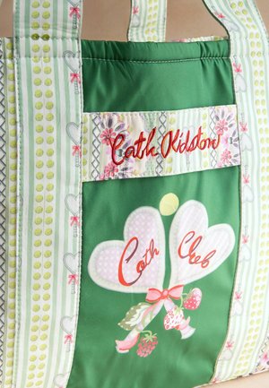 Zelená látková taška s kvetinovými a srdcovými vzormi, červeným vyšívaným nápisom "Cath Kidston" a dvoma balónmi v tvare srdca s nápisom "Cath Club".