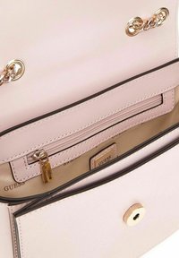 Sac à main en cuir rose clair avec des accessoires en métal doré. L'intérieur comprend une poche zippée et une étiquette de marque, avec des lignes lisses et épurées et une texture minimale.