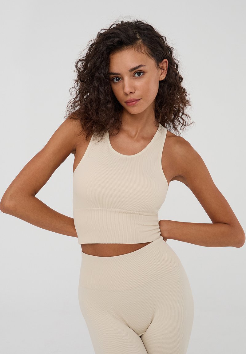 Crop top a coste beige con scollatura rotonda e spalline larghe, abbinato a leggings a coste coordinati con vita alta.