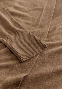 Brown knit sweater featuring a ribbed cuff and a soft, textured fabric, designed with a relaxed fit and subtle diagonal seam details.