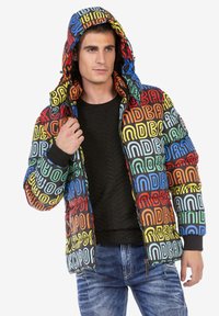 Kleurige gewatteerde jas met een grafische print van verschillende hoofdletters in rood, blauw, geel en groen op een zwarte achtergrond.