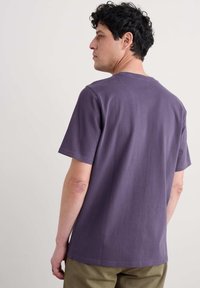 Fialové bavlněné tričko s kulatým výstřihem a krátkým rukávem, s hladkým povrchem a rovnem zakončením. Nosené s khaki kalhotami.