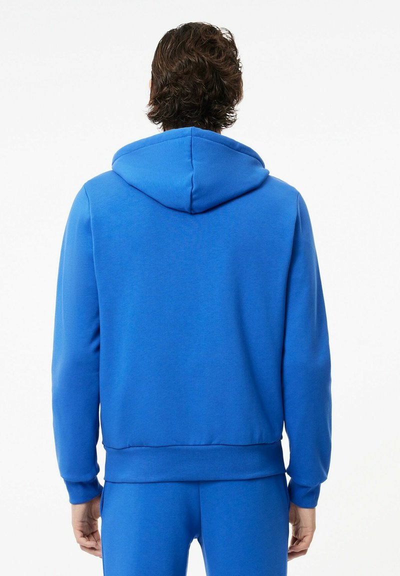 Felpa blu in cotone con cappuccio regolabile, polsini e orlo a costine. Tessuto morbido e forma leggermente aderente. Vista posteriore mostrata.