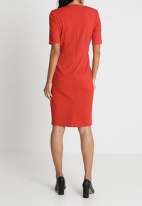 Czerwona, dopasowana sukienka do kolan z elastycznego materiału, z krótkimi rękawami i zamek błyskawiczny z tyłu. Posiada detal szwu wzdłuż pleców.